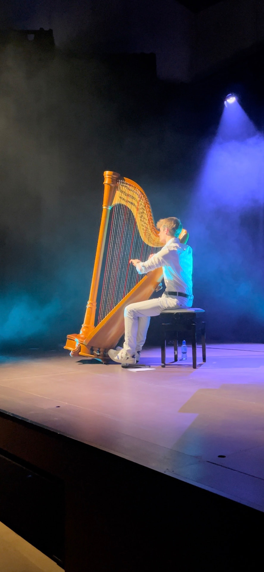 François Moriau jouant de la harpe sous les éclairages bleus au Centre culturel d'Aubel